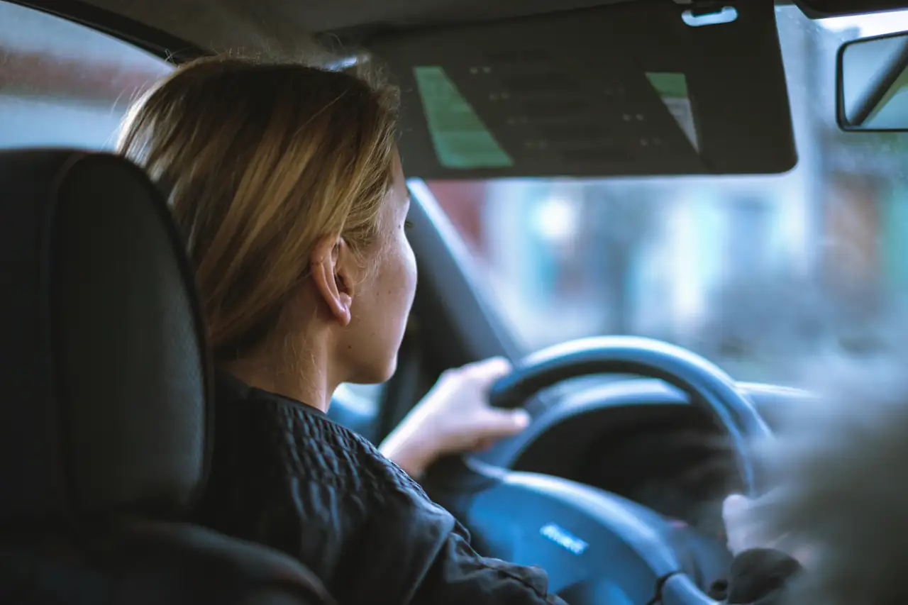 Mulher dirigindo um carro numa rua da cidade.