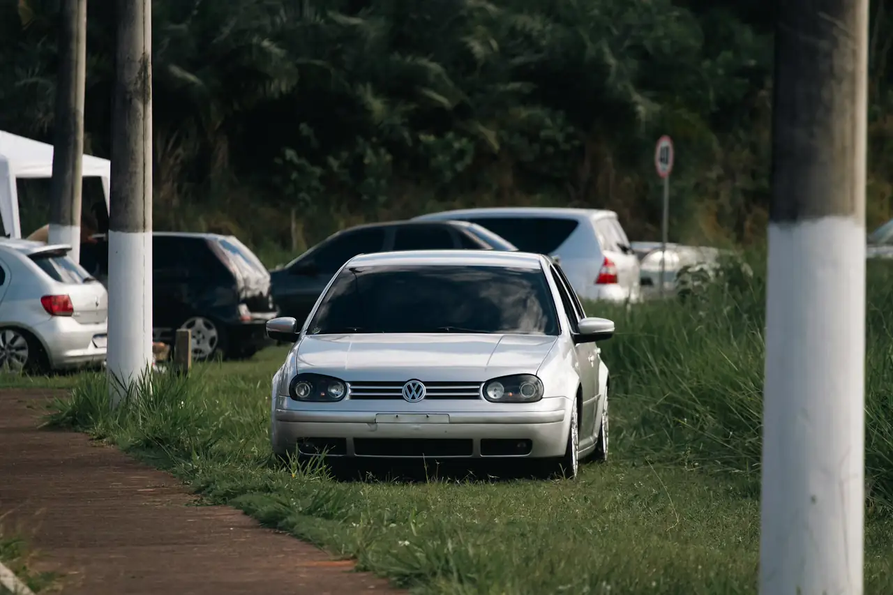 Hatch prata estacionado na grama ao lado de outros carros usados.