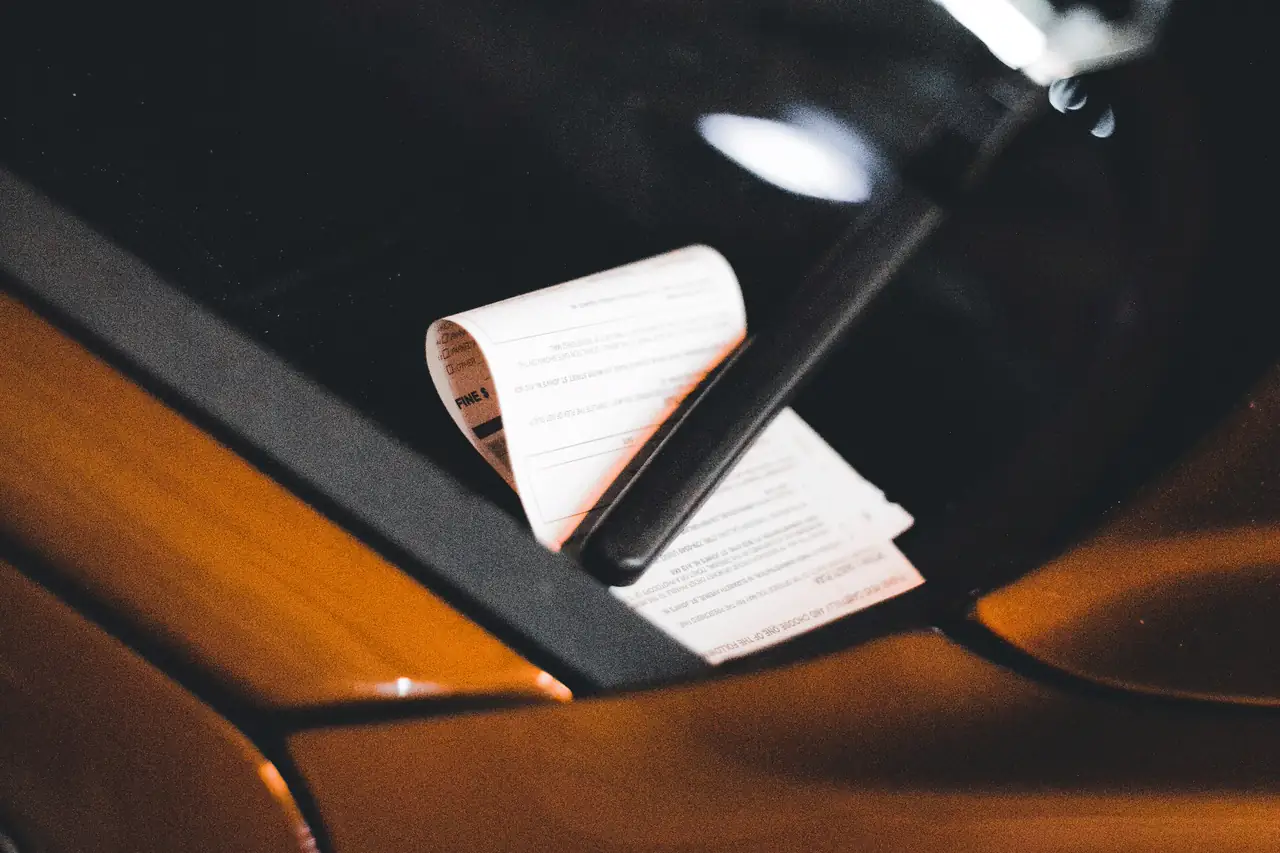 Papel de notificação preso no limpador do para-brisa de um carro.