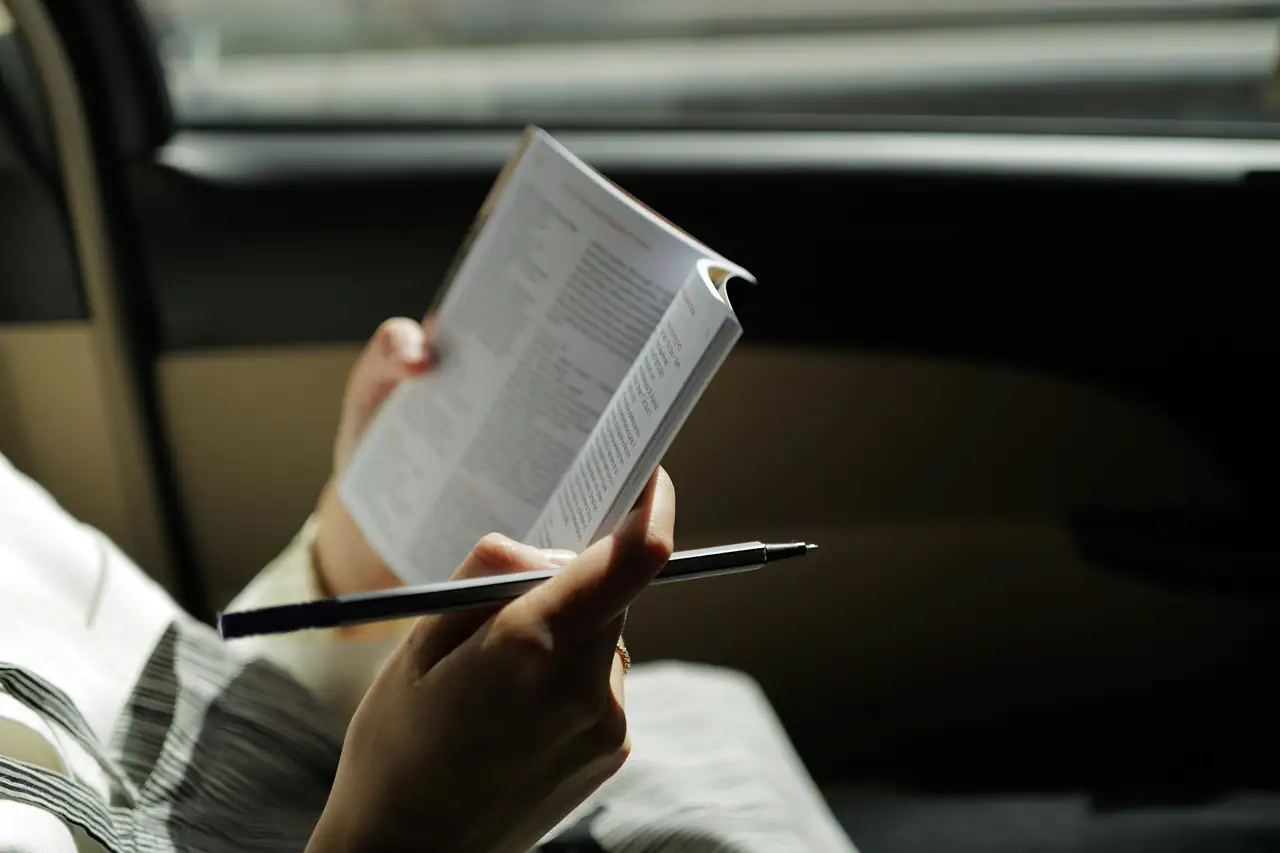 Pessoa lendo um livreto dentro de um carro, com uma caneta na mão.