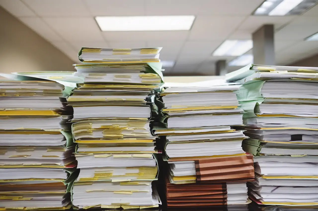 Pilhas de pastas e documentos sobre uma mesa de escritório.