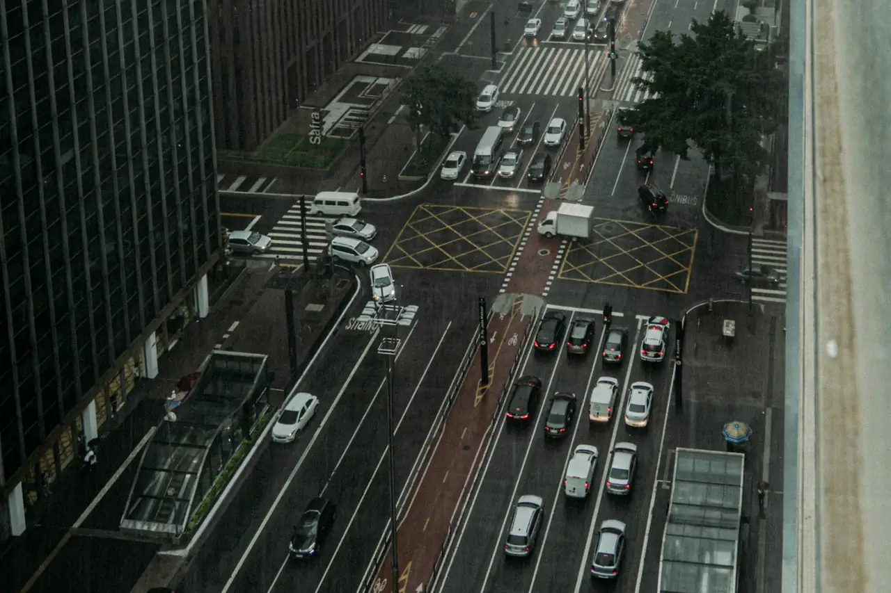 Avenida movimentada de São Paulo vista do alto, com faixas de pedestre e carros parados no semáforo.