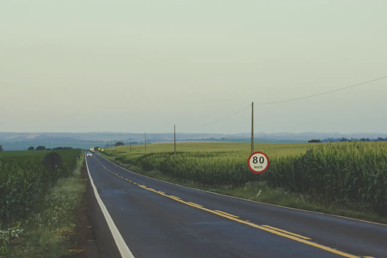 Rodovia de pista simples entre plantações, com placa de limite de 80 km/h.