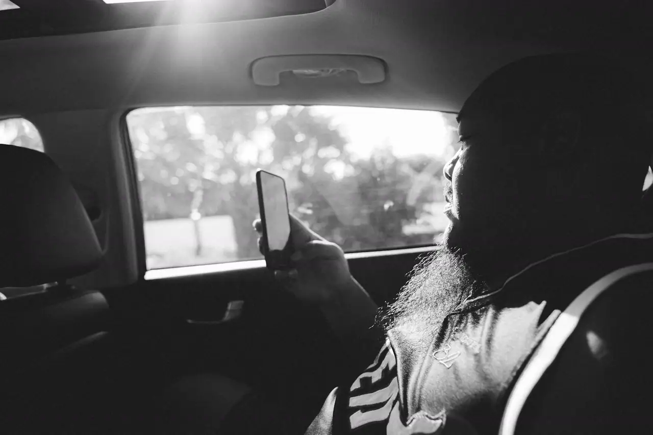 Homem conferindo o celular no banco de trás de um carro, em preto e branco.