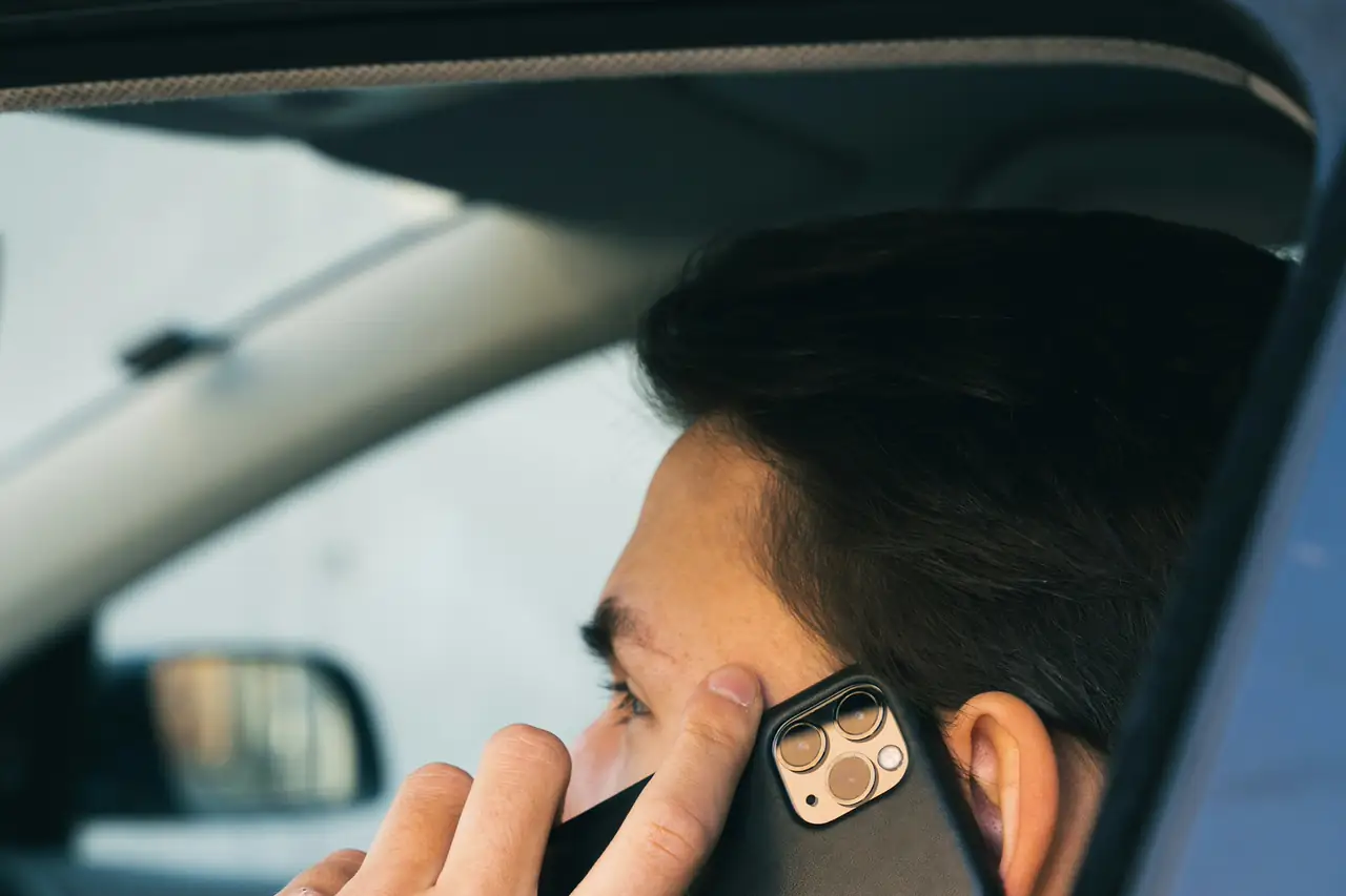 Homem falando ao celular dentro de um carro.