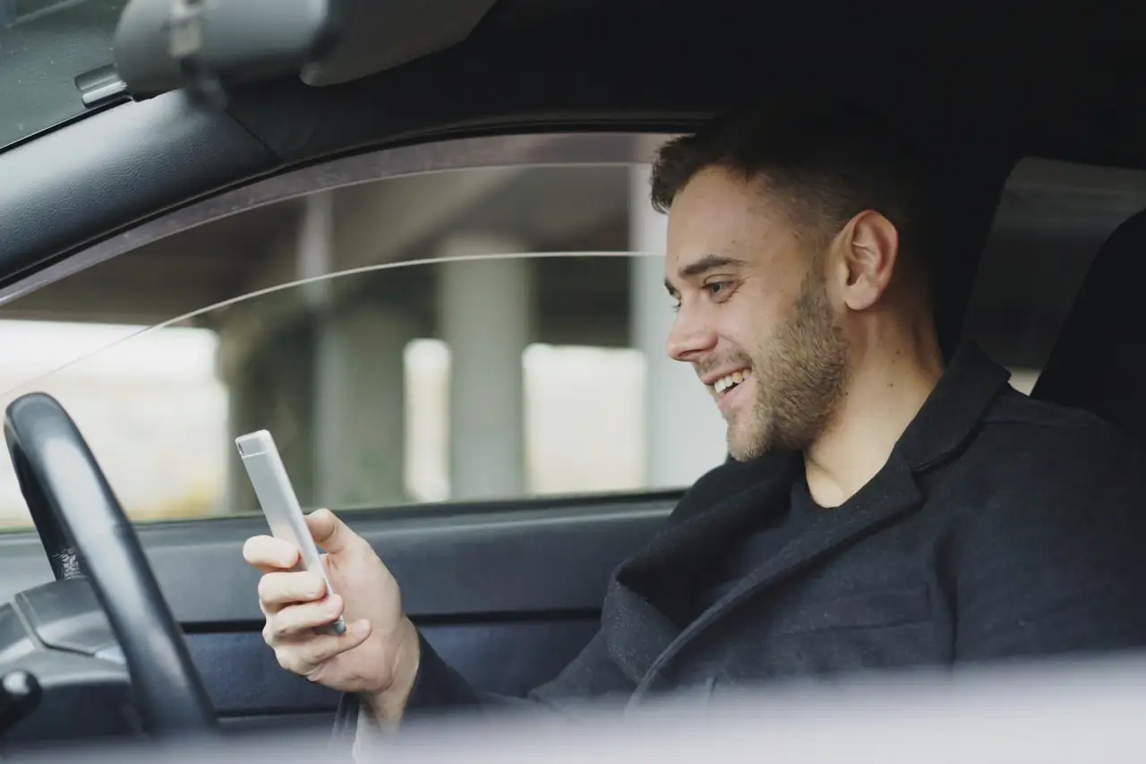 Homem sorrindo enquanto olha o celular sentado ao volante.