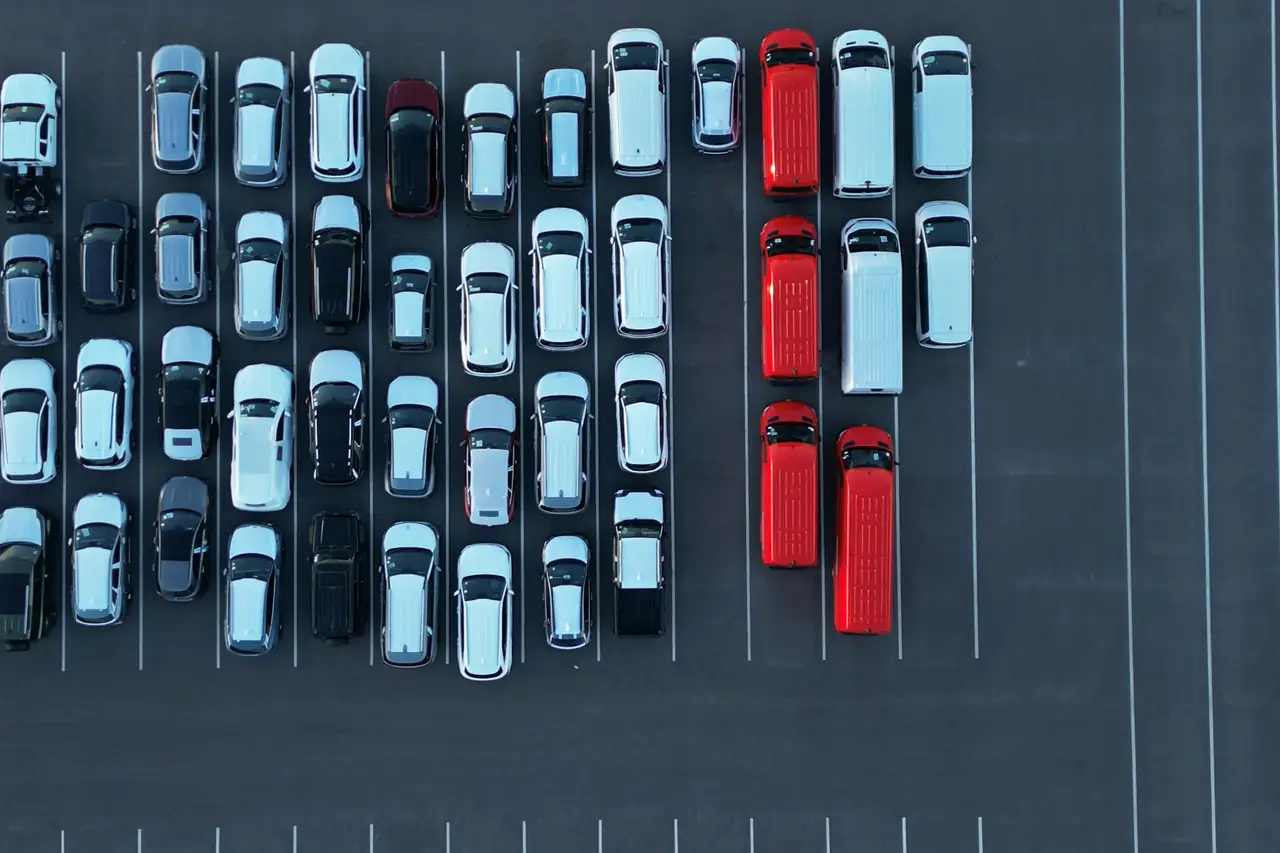 Vista aérea de um pátio com fileiras de carros brancos, pretos e vermelhos.