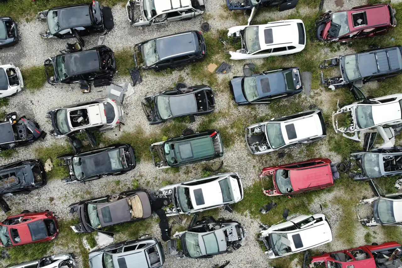 Vista aérea de um ferro-velho com carros desmontados e batidos sobre o cascalho.