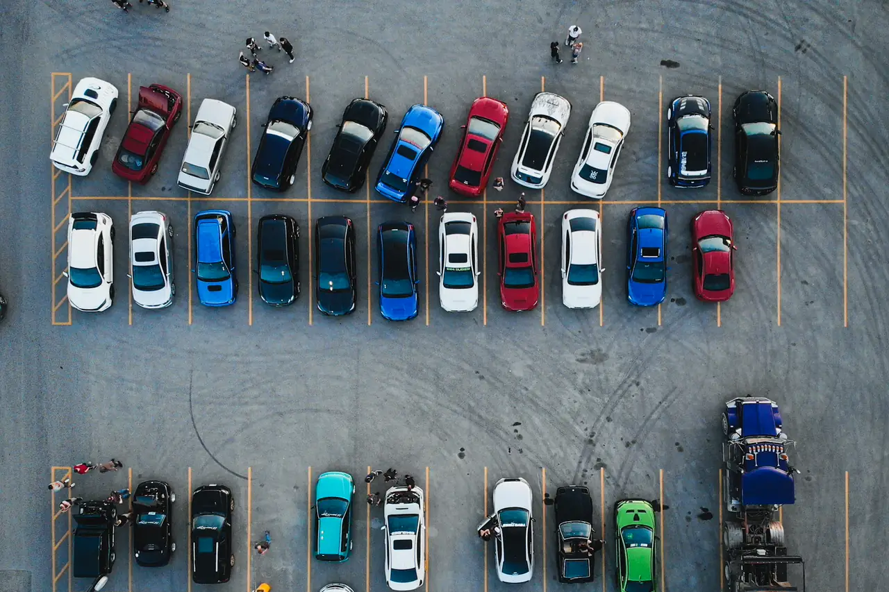 Carros de várias cores estacionados em vagas, vistos de cima.