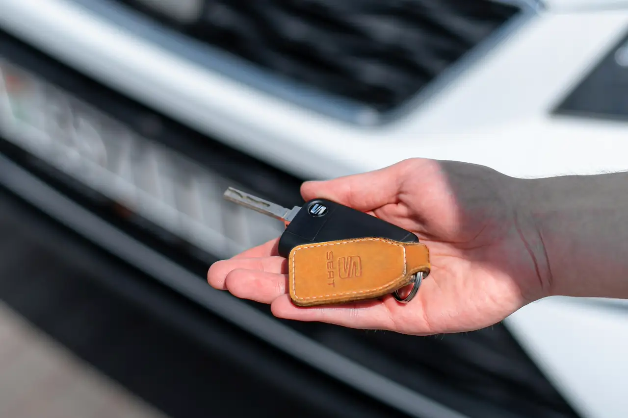 Mão estendida segurando a chave de um carro, com o veículo ao fundo.