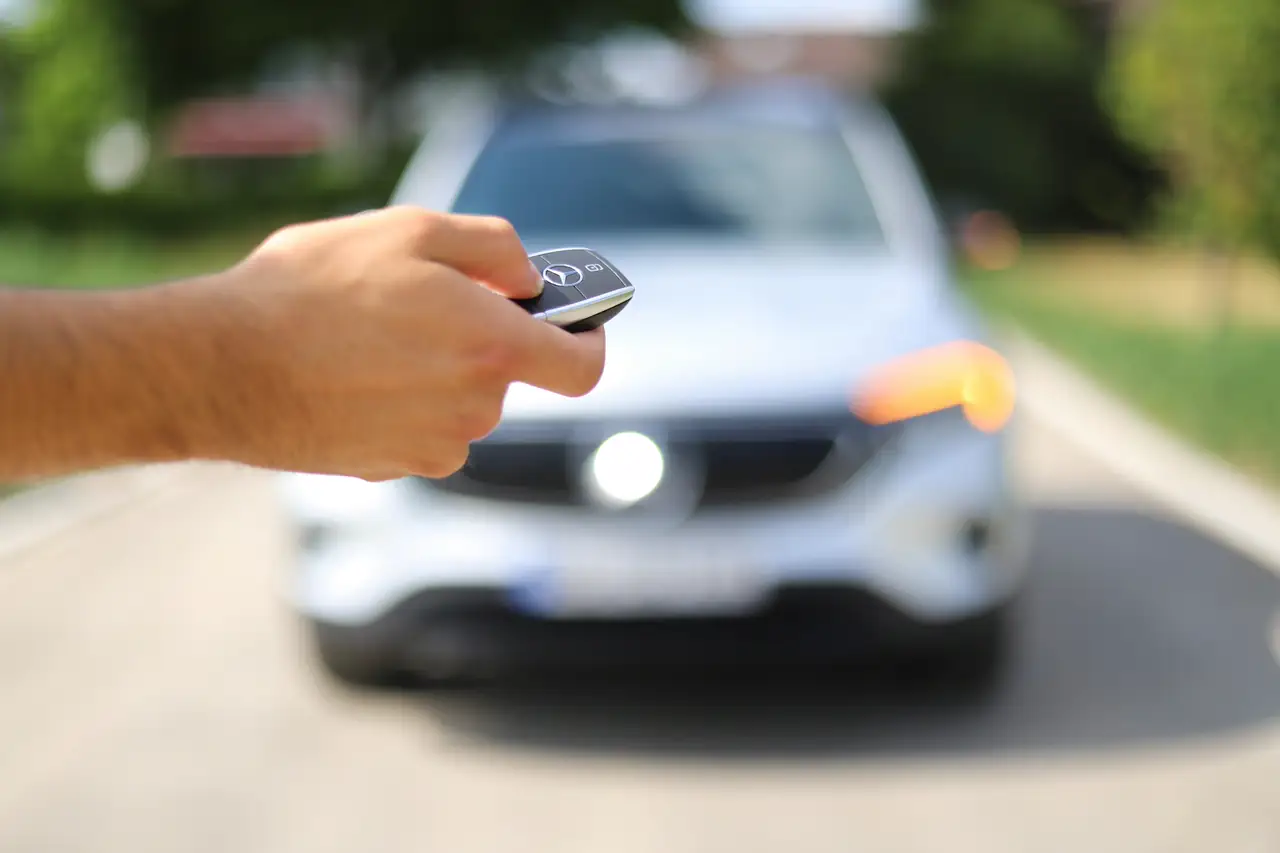 Mão apontando a chave para um SUV prateado desfocado ao fundo.