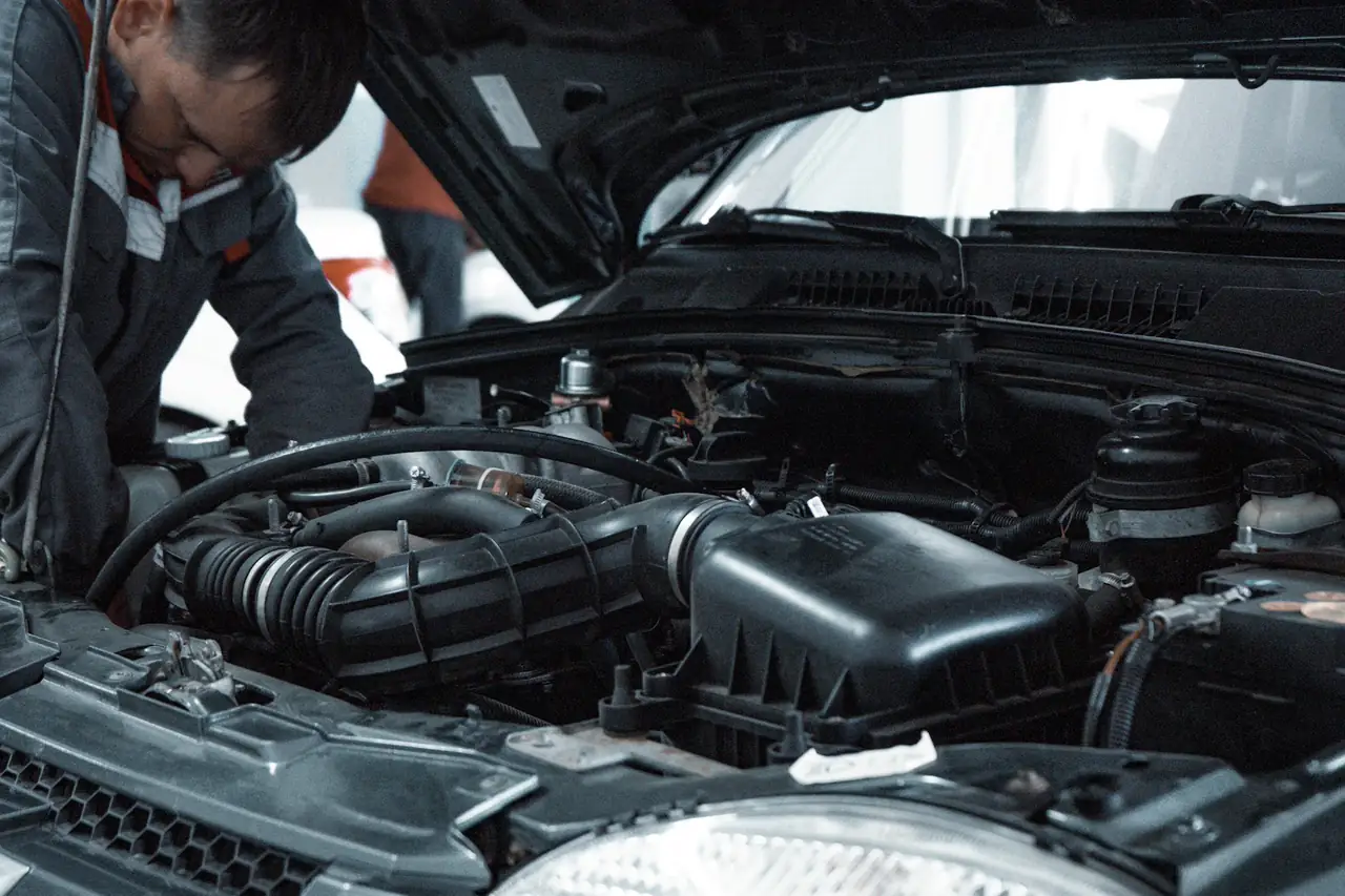 Mecânico de uniforme inspecionando o motor de um carro com o capô aberto.