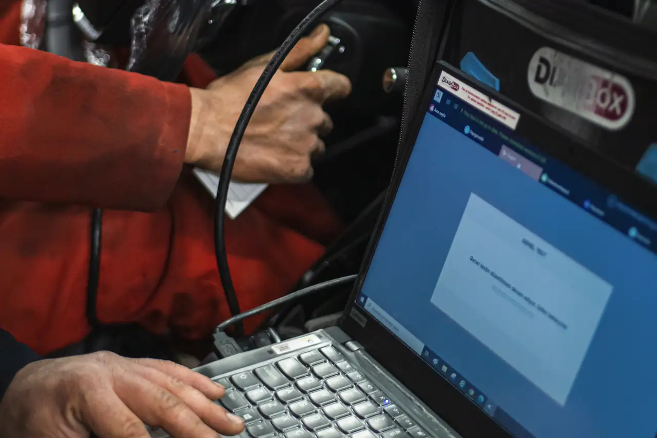 Técnico conectando um aparelho de diagnóstico ao carro, com o notebook aberto ao lado.