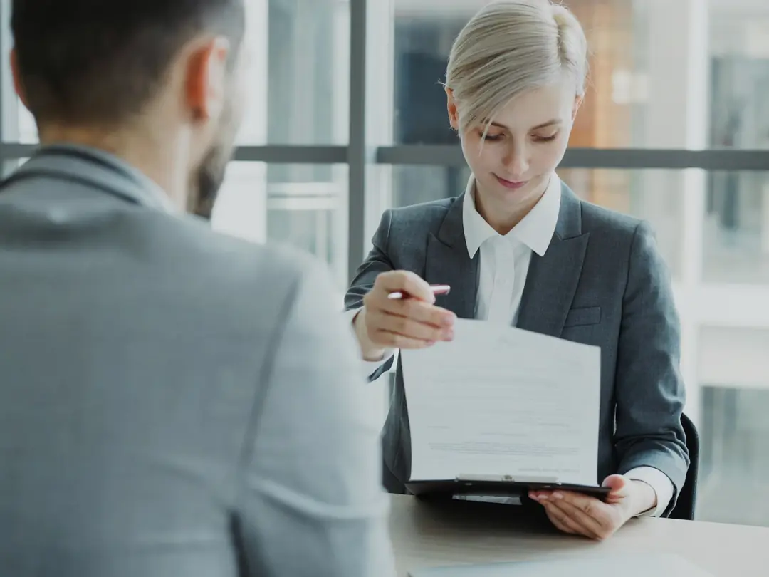 Atendente mostrando um documento a um cliente numa mesa de escritório.