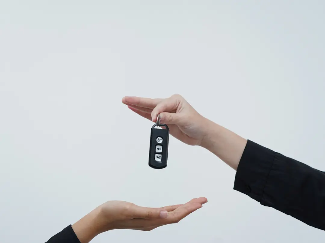 Uma mão entregando a chave de um carro para outra pessoa, sobre fundo claro.
