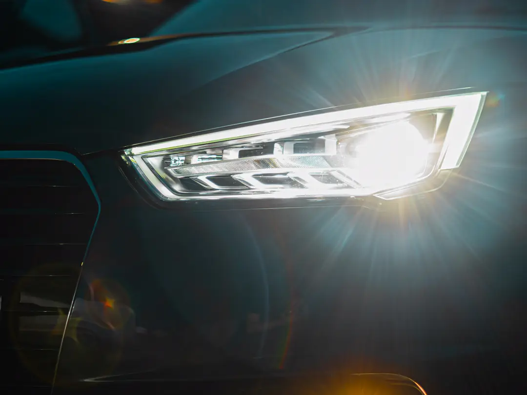 Detalhe do farol aceso de um carro escuro, à noite.