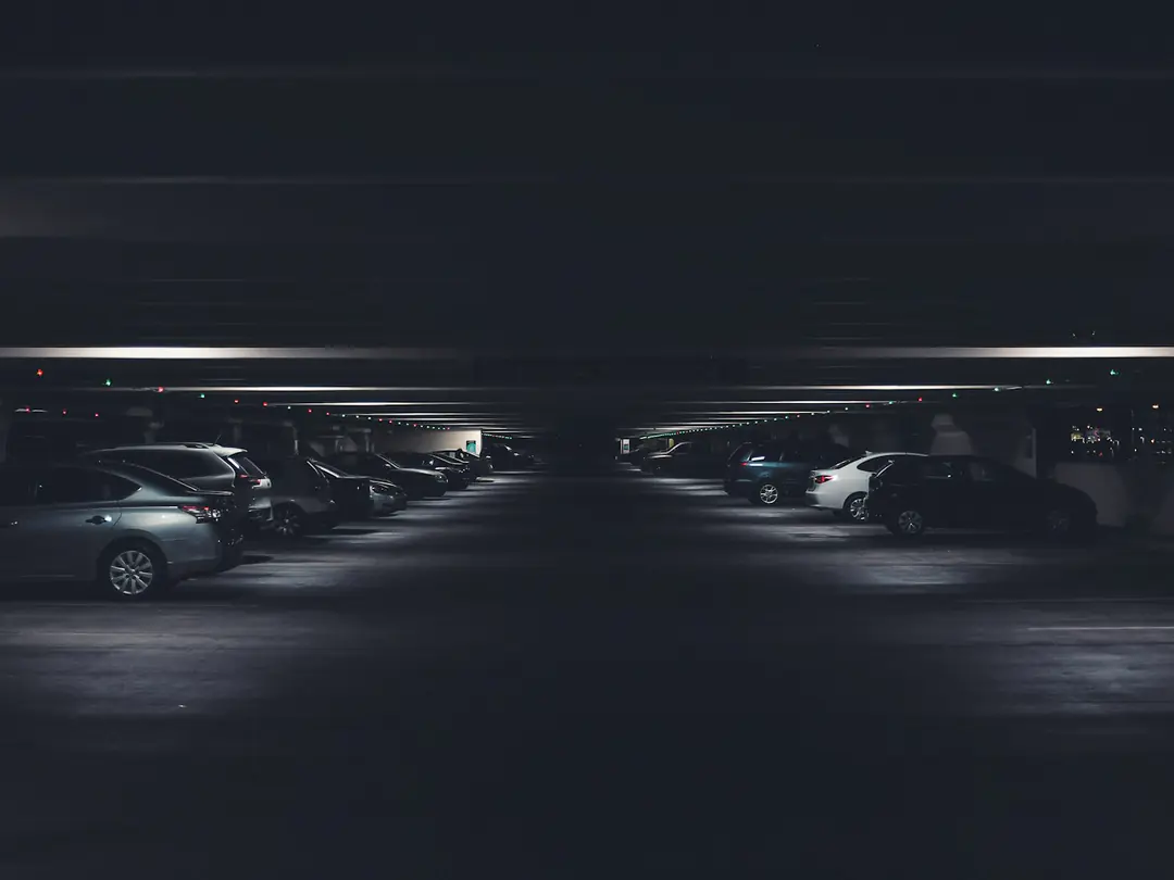 Garagem subterrânea pouco iluminada, com carros estacionados nas duas laterais.