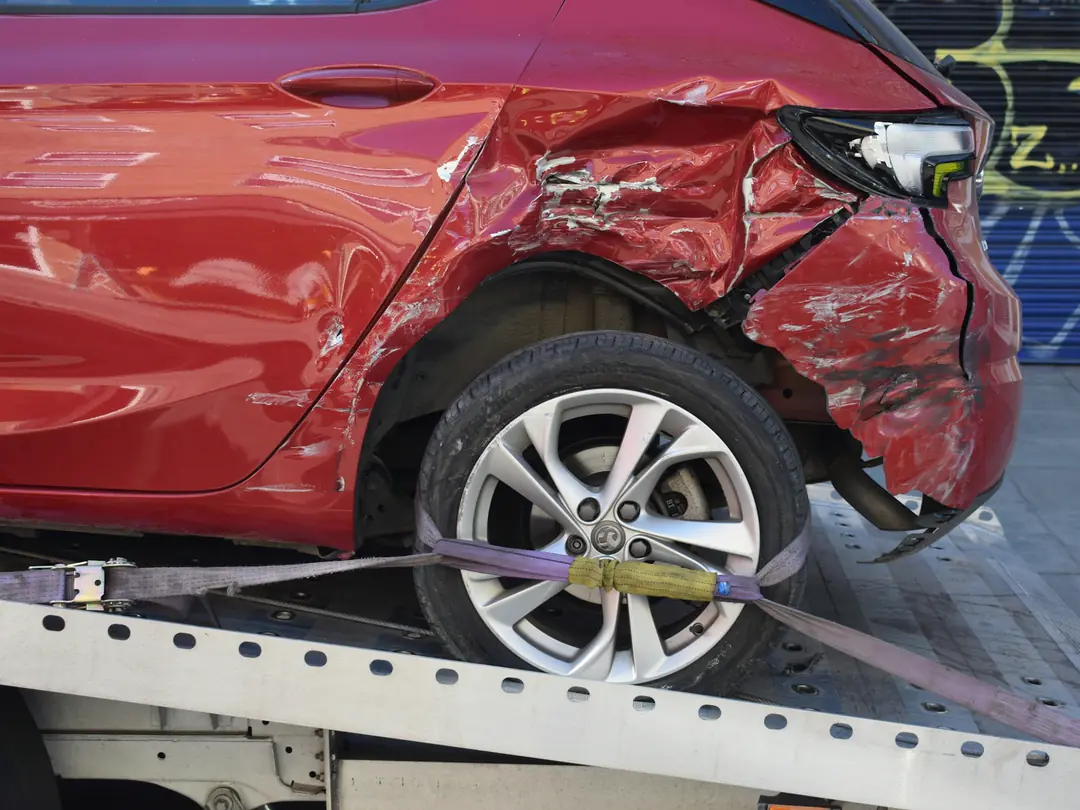 Carro vermelho com a lateral traseira amassada, preso à plataforma de um guincho.