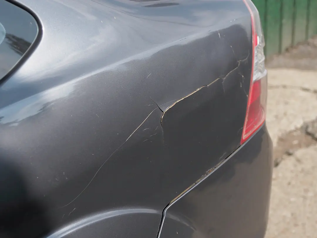Lateral traseira de um carro cinza com a lataria riscada e amassada.