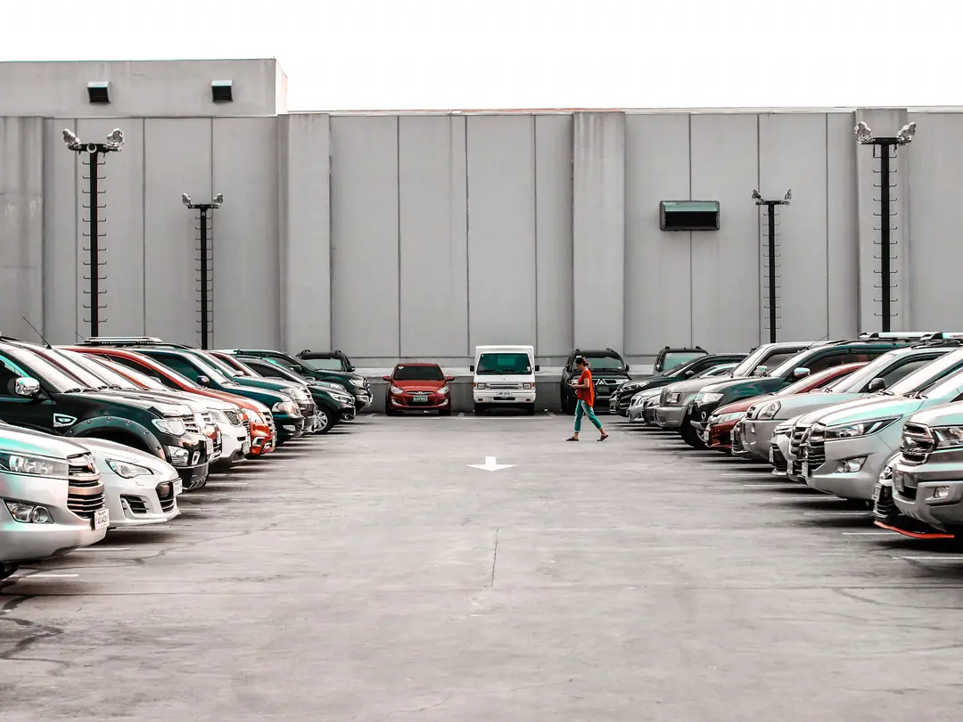 Pátio coberto com duas fileiras de carros usados estacionados e uma pessoa caminhando entre eles.