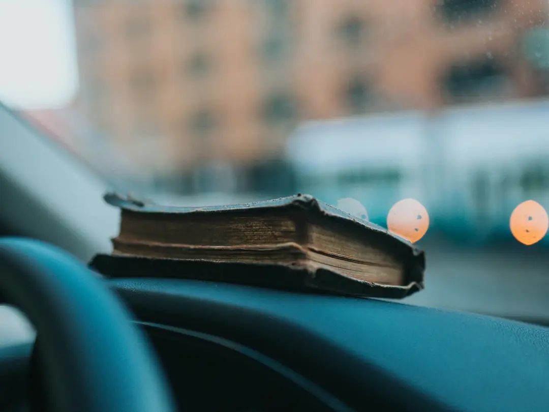 Livro antigo apoiado sobre o painel de um carro, com a rua desfocada ao fundo.