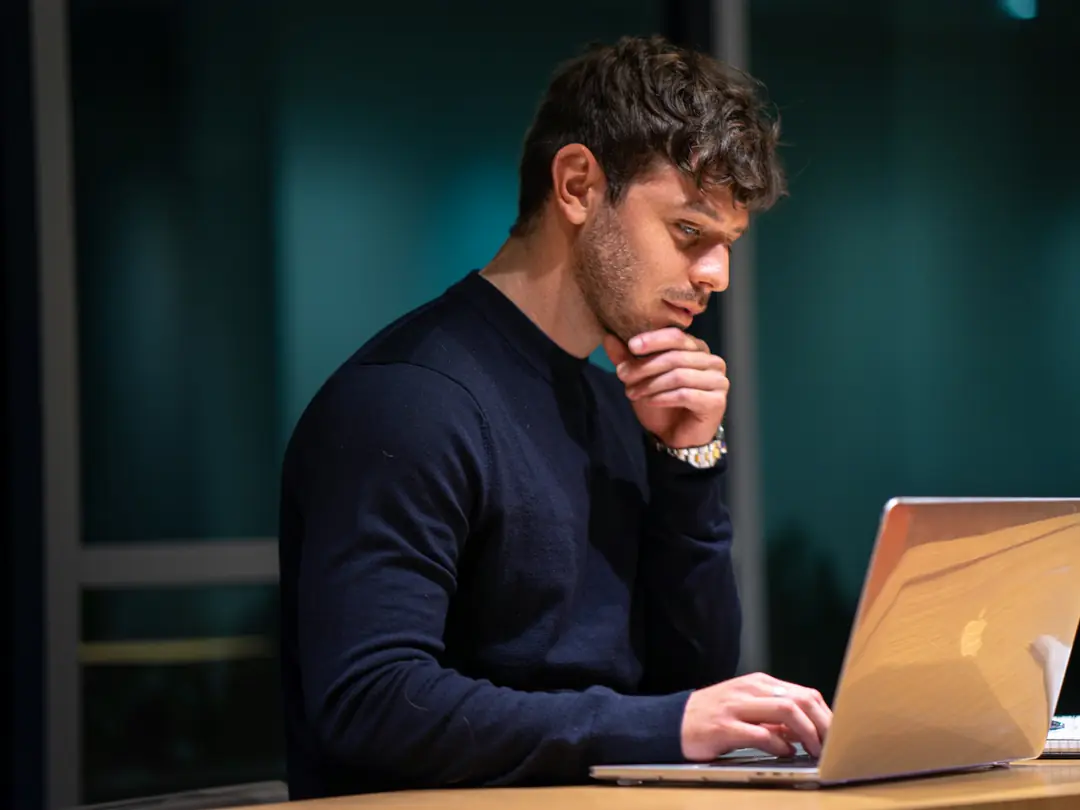 Homem pensativo diante de um notebook, comparando informações.