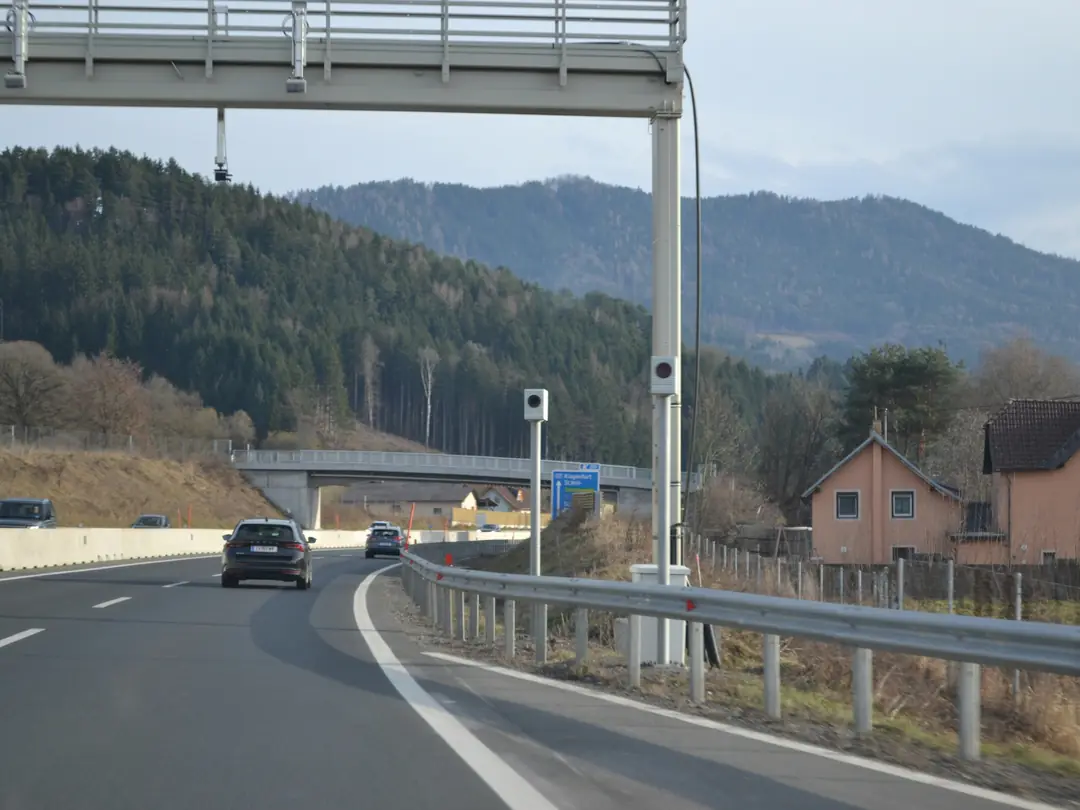 Rodovia com pórtico e radar de velocidade à beira da pista, carros ao fundo.