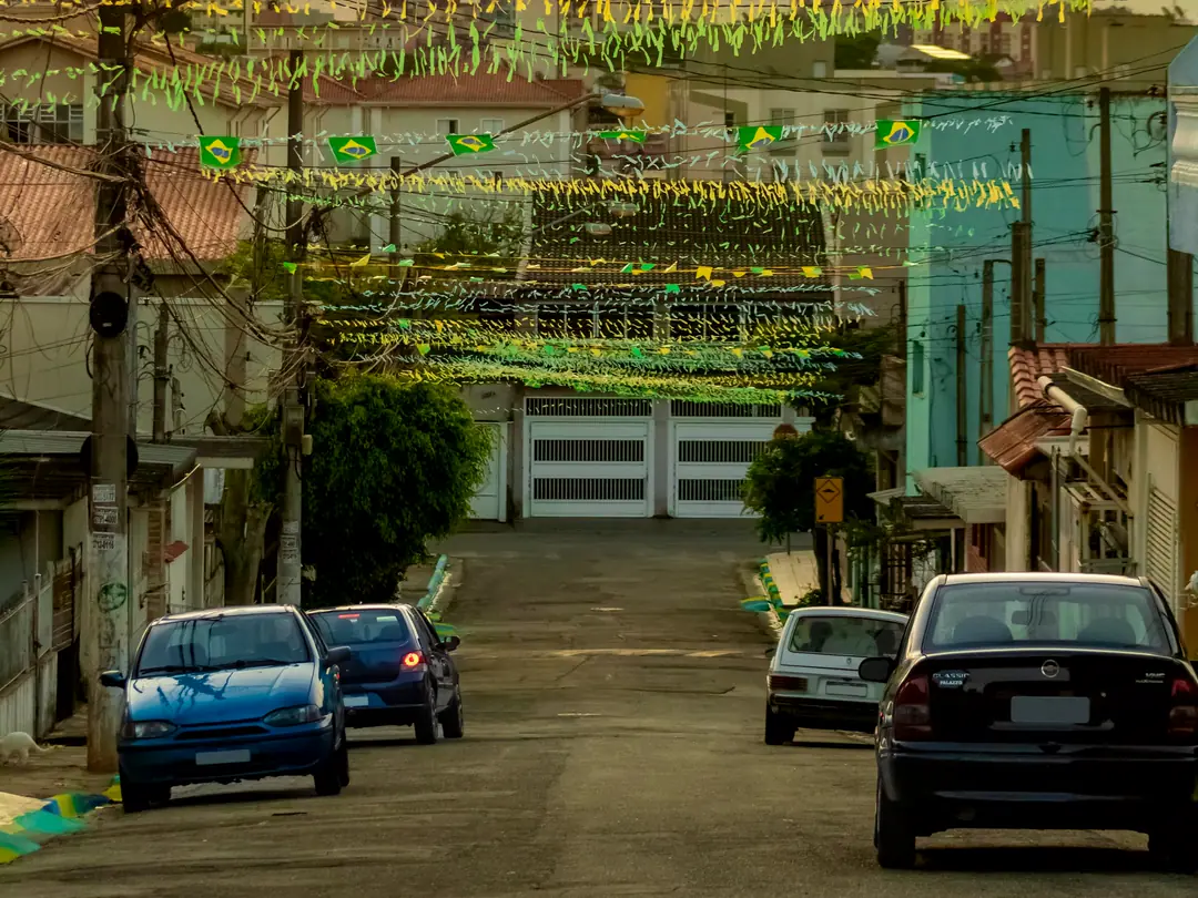 Rua residencial brasileira enfeitada com bandeirinhas verde e amarelo, com carros estacionados.