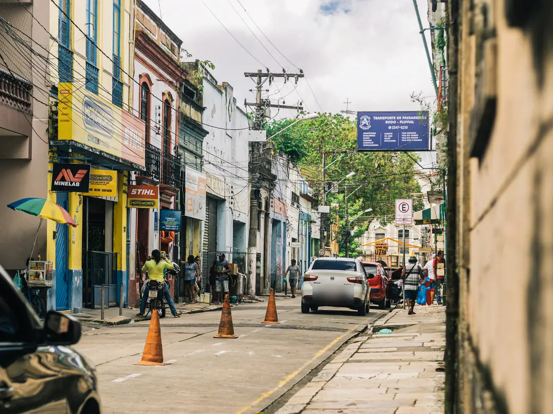 Rua comercial do centro de uma cidade brasileira, com lojas, cones e carros estacionados.