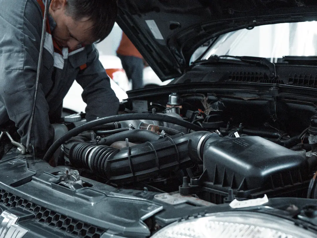 Mecânico de uniforme inspecionando o motor de um carro com o capô aberto.