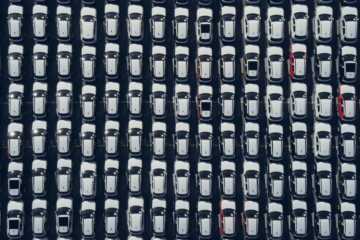 Pátio visto de cima, com fileiras de carros brancos estacionados em ordem.
