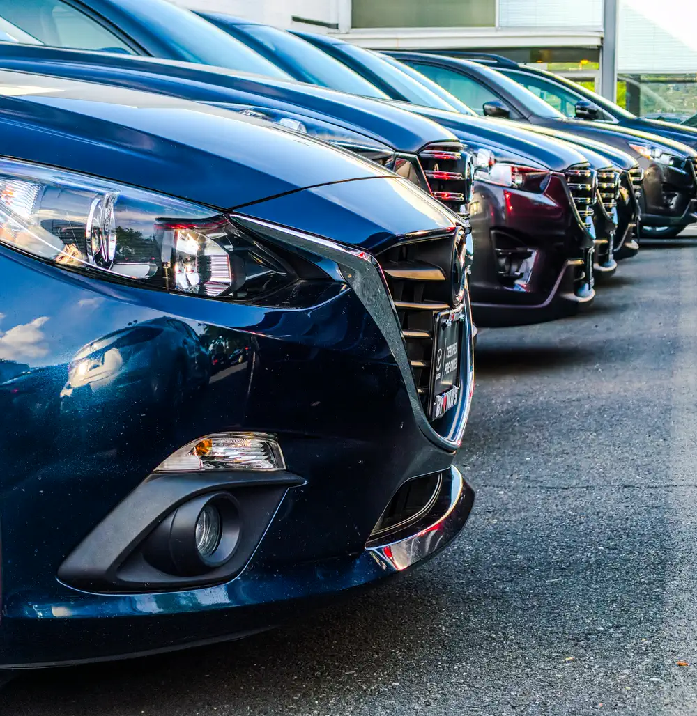 Fileira de carros usados estacionados lado a lado num pátio.